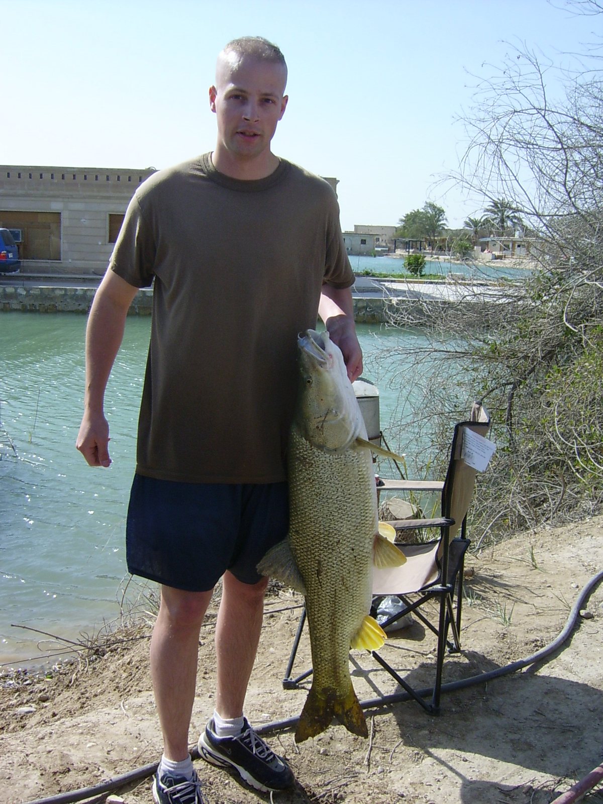 A soldier holds up a big fish he caught in one of the moats at Camp Slayer, 2003.